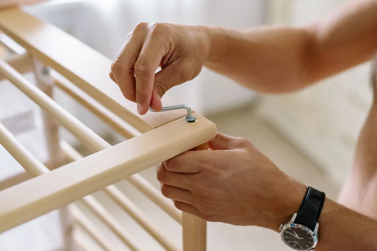 Hands using an Allen key to assemble flat-pack timber furniture indoors