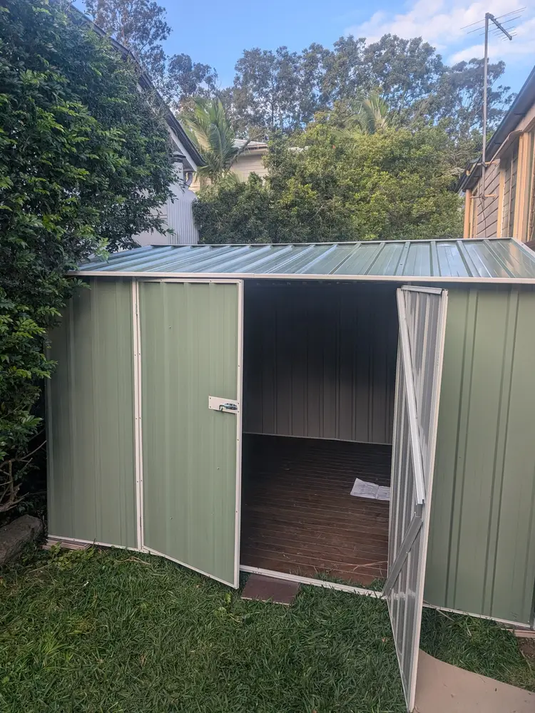 Green steel garden shed, freshly assembled in a backyard with its doors open