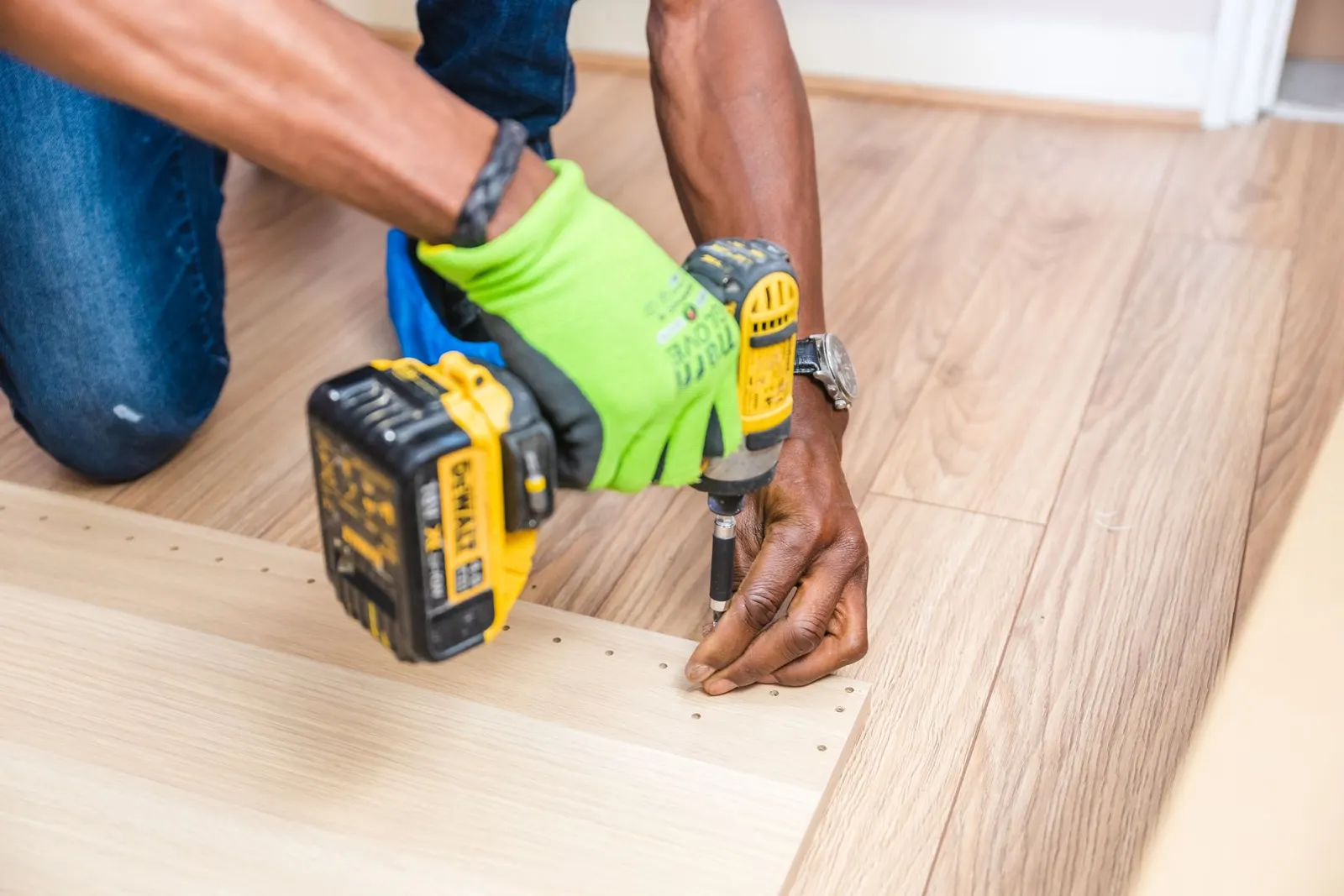 Hands using a cordless drill to assemble flat-pack furniture on a timber floor