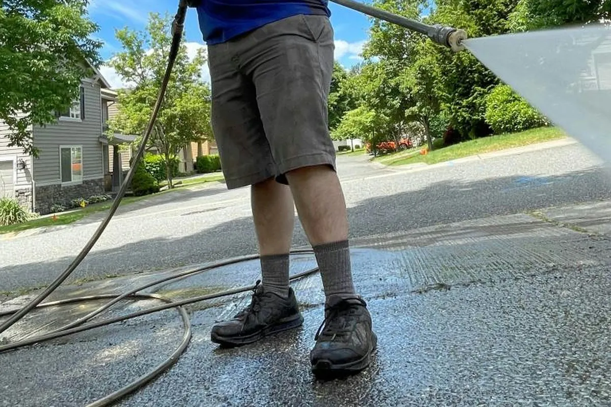 Driveway being pressure washed at a suburban home, the cleaned strip still wet