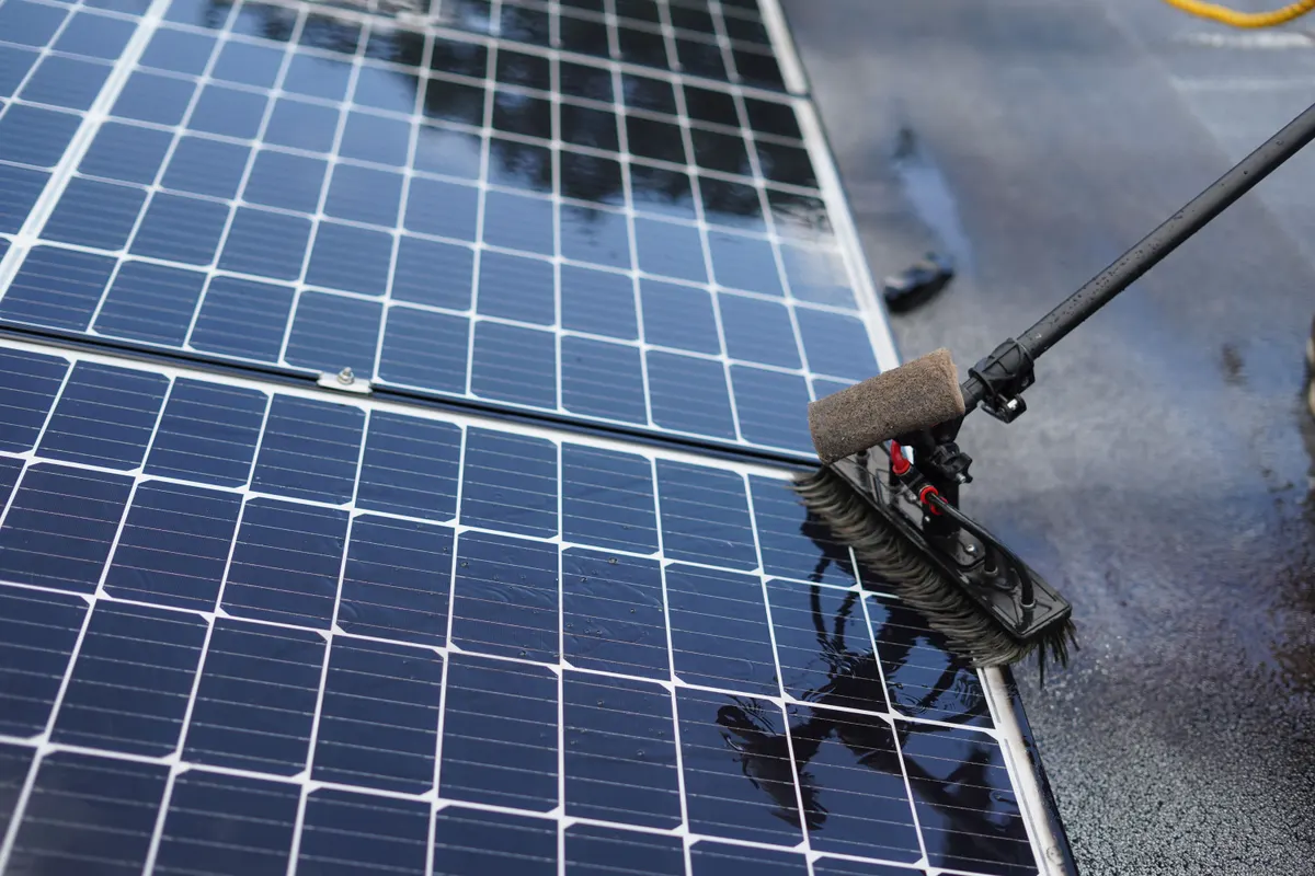 Solar panels being cleaned with a soft, water-fed brush on an extension pole
